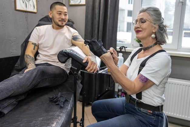 Mestre de tatuagem feminina madura trabalhando com o cliente