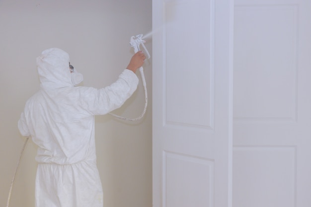 Mestre pintando portas de madeira com pistola de pintura de processamento