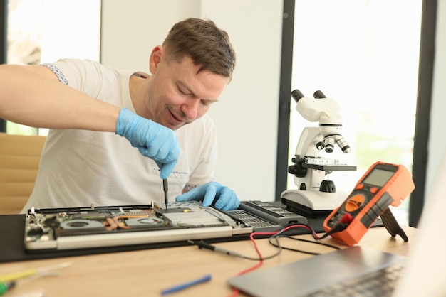 Mestre positivo desaparafusa pequeno detalhe de laptop quebrado sentado em mesa de madeira homem habilidoso