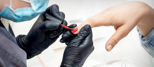 Mestre profissional de manicure pintando unhas femininas com esmalte vermelho em salão de beleza