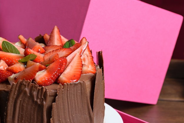 Metade de um bolo de chocolate com morangos, folhas de manjericão, geleia de amora e placas de chocolate ao redor.