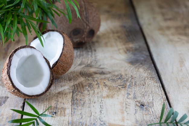 Foto metade de um coco e um galho de palmeira estão sobre uma mesa de madeira. copie o espaço