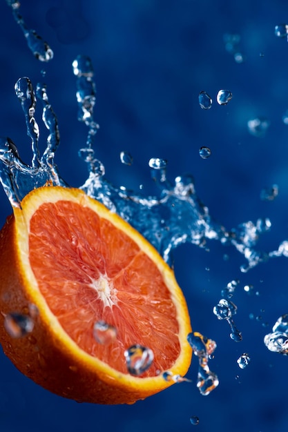 Metade de uma laranja cai sobre um fundo azul com gotas de água