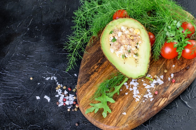 Metade do abacate cetogênico recheado com molho de atum nad. Tomate cereja, endro e rúcula na tábua de madeira. Dieta cetogênica saudável.