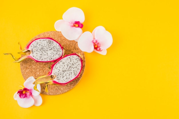 Foto metade fruta do dragão na porta-copos de cortiça com flor de orquídea rosa em pano de fundo amarelo