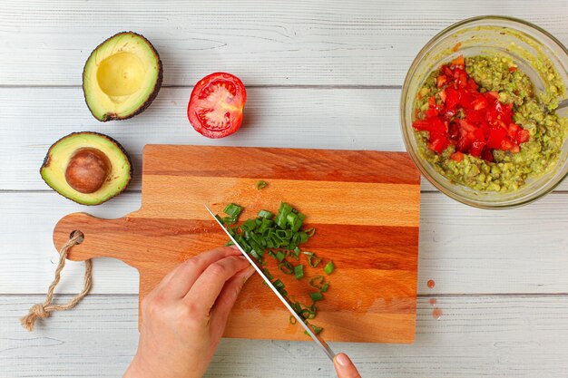 Metades de abacate, tomate, cebolinha cortada à mão - ingredientes básicos de guacamole na mesa de trabalho, vista de cima