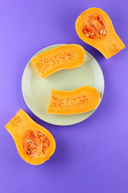 Metades de abóbora suculenta laranja em um prato branco sobre um fundo roxo Vista de cima Conceito de comida vegetariana Closeup