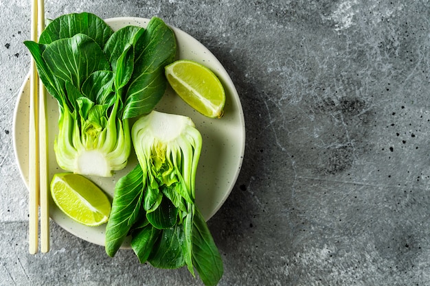 Metades de bok choi bebê, limão, pauzinhos no fundo cinza