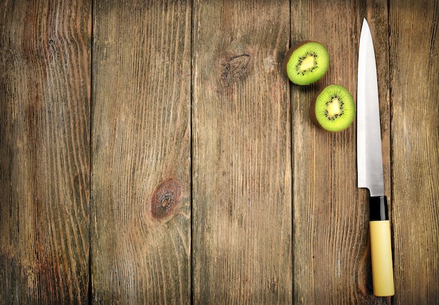Metades de kiwi com faca em fundo de madeira