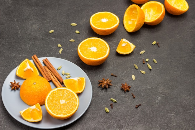 Metades de laranja, paus de canela e anis estrelado na placa cinza. Especiarias na mesa. Laranjas e cascas na mesa. Fundo preto. Copie o espaço. Vista do topo.