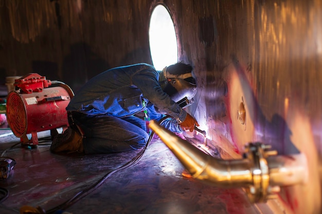 El metal reparado masculino del trabajador del argón del arco de soldadura está soldando el aceite inoxidable del tanque de la construcción industrial de las chispas dentro de los espacios confinados.