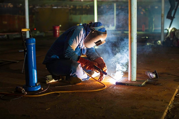 Foto el metal de los trabajadores de soldadura es parte de la construcción de la parte inferior de la placa del tanque de maquinaria del tanque de almacenamiento de petróleo y gas