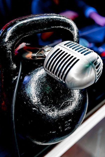Metall-Vintage-Mikrofon liegt auf einer schwarzen Sport-Kettlebell in der Institution. Foto in hoher Qualität