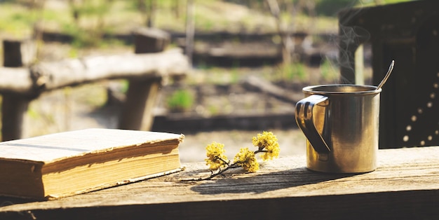 Foto metallbecher, blühender zweig und ein buch auf einem holztisch im garten