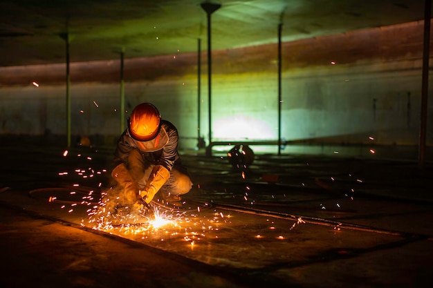 Metallschneidender Funke des männlichen Arbeiters auf der Stahlplatte des Tankbodens mit Blitz des Schneidlichts aus nächster Nähe. Tragen Sie Schutzhandschuhe und Maske in seitlich beengten Räumen