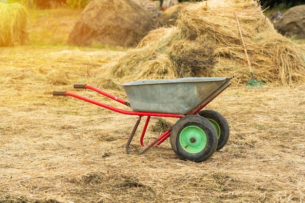 Metallschubkarre auf dem Hintergrund von Heuhaufen, das Konzept der Landwirtschaft