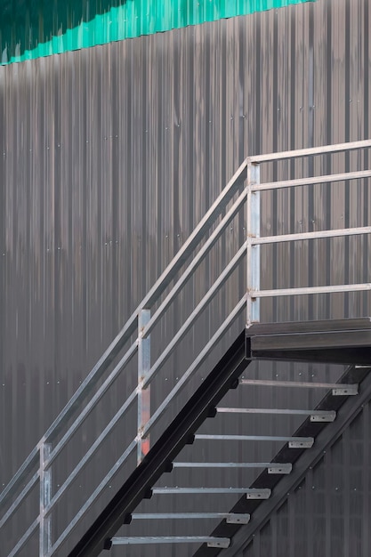 Metalltreppe auf grauer und grüner Wellblechwand des Lagergebäudes auf der Baustelle