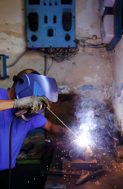 Metalúrgico com luvas de soldagem e máscara trabalhando com uma máquina de solda em um worksho familiar