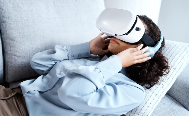 Metaverso VR e jogos com uma mulher negra em um sofá na sala de estar de sua casa AI 3D e realidade virtual com uma jovem jogadora usando um fone de ouvido para acessar o ciberespaço para um videogame