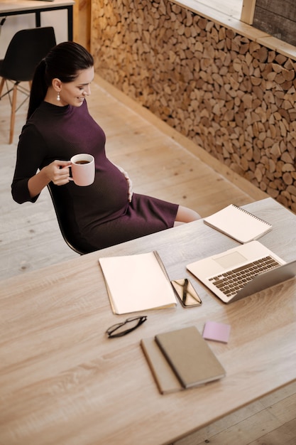 Meu melhor trabalho. Vista superior de uma mulher de negócios alegre e positiva, sentada enquanto abraça sua barriga e olhando para baixo