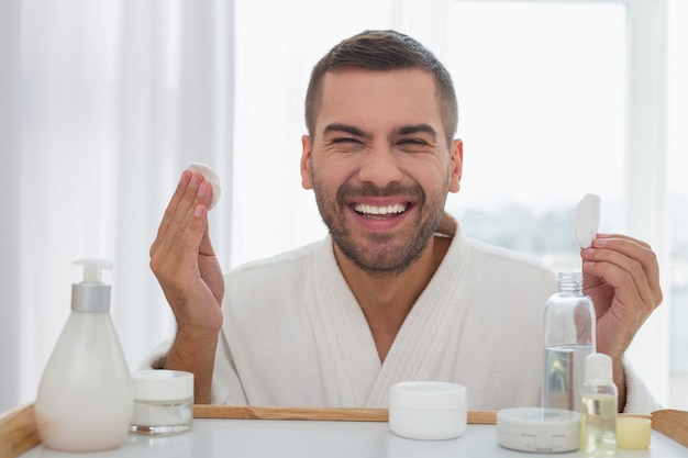 Meu rosto. homem feliz e alegre olhando no espelho enquanto segura almofadas de algodão nas mãos