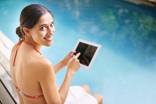 Meu tablet vai a todos os lugares comigo Foto de uma jovem relaxando à beira da piscina com seu tablet