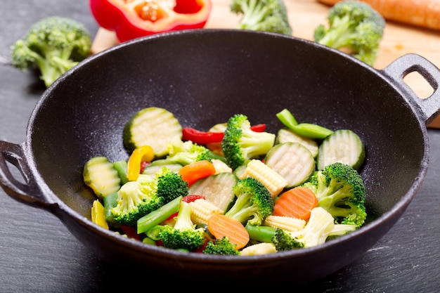 Mexa os vegetais fritos em uma wok na mesa escura