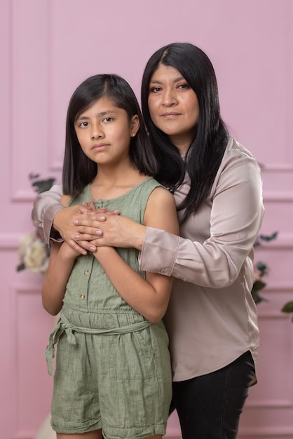 Mexicana mãe e filha abraçando no fundo rosa isolado