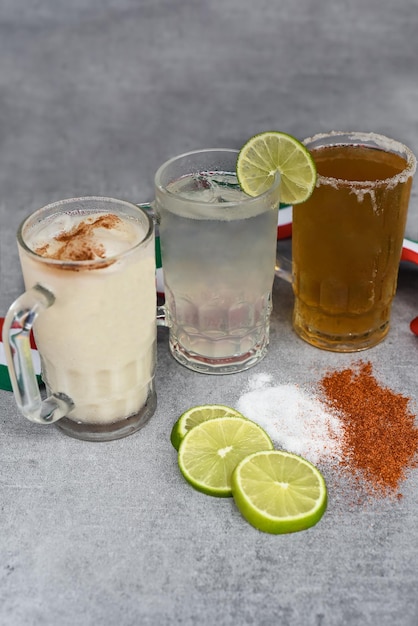 Foto mexicano bebe água horchata, suco de limão e cerveja em uma mesa cinza com sal, pimenta e limão