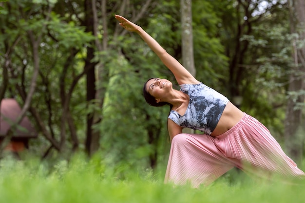 Mexikanerin beim Yoga mit verschiedenen Körperhaltungen im Outdoor-Park mit Gras und Bäumen im Hinter...