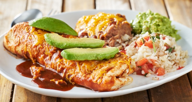 Mexikanische Burritoplatte mit roter Enchiladasauce, gebratenen Bohnen, Reis und Guacamole