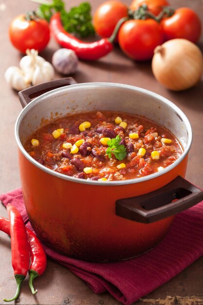 Foto mexikanische chili con carne im roten rustikalen topf mit zutaten