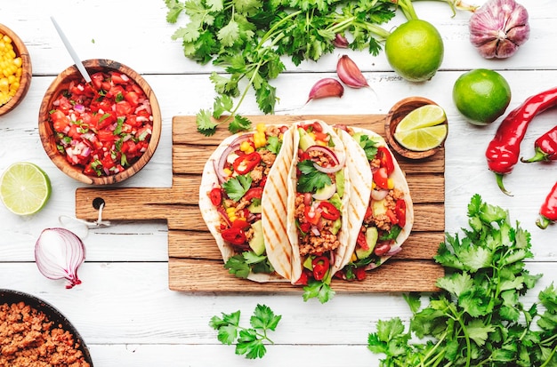 Mexikanische Küche Tacos mit Rindfleisch, Mais, roten Bohnen, Tomaten-Salsa-Sauce und Zwiebeln in Maistortilla an Bord Draufsicht auf den weißen Tischhintergrund