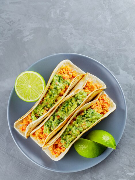 Mexikanische Nahrung. Tacos mit gebratenem Hackfleisch und Guacamole auf einem grauen Teller. Mexikanische Tacos und Limettenscheiben auf grauem Hintergrund. Platz kopieren. Ansicht von oben