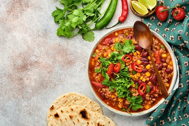 Mexikanische schwarze Bohnensuppe mit Hackfleisch, Tomate, Koriander, Avocado und Gemüseeintopf auf hellgrauem Schiefer-, Stein- oder Betonhintergrund. Traditionelles mexikanisches Gericht. Draufsicht mit Kopienraum.