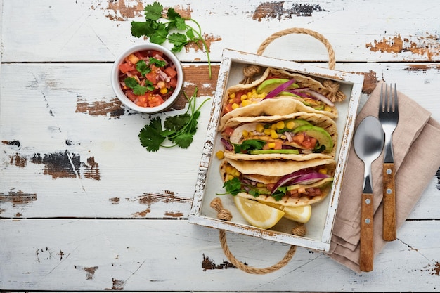 Mexikanische Tacos mit gegrilltem Hähnchen, Avocado, Maiskörnern, Tomate, Zwiebel, Koriander und Salsa alter weißer Holztisch. Traditionelles mexikanisches und lateinamerikanisches Street Food. Ansicht von oben.