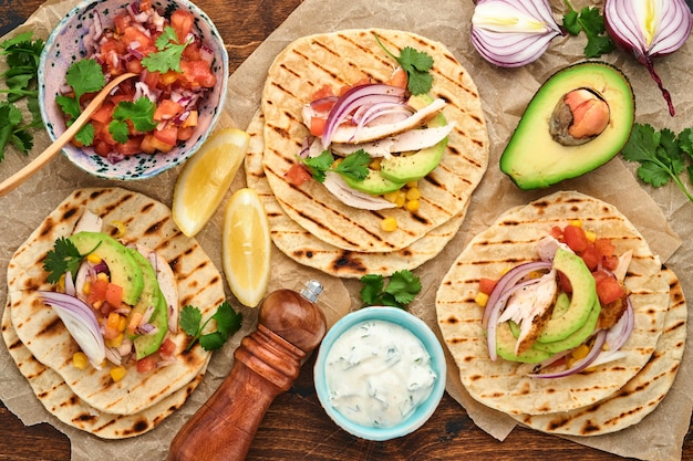 Mexikanische Tacos mit gegrilltem Huhn, Avocado, Maiskörnern, Tomaten, Zwiebeln, Koriander und altem Holztisch der Salsa. Traditionelles mexikanisches und lateinamerikanisches Streetfood. Ansicht von oben.