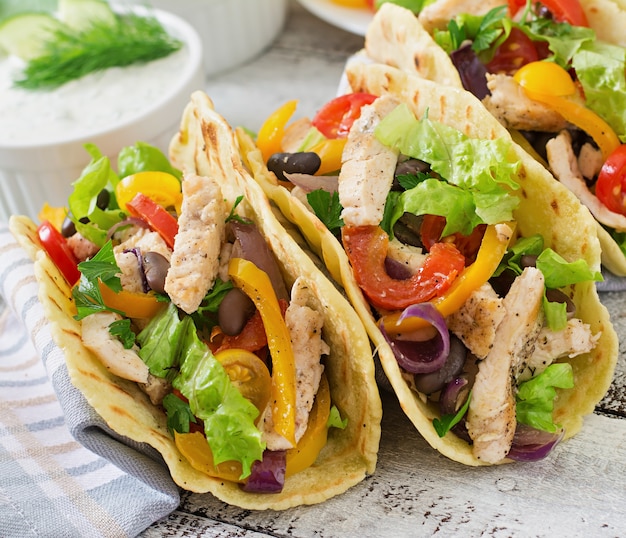 Mexikanische tacos mit hühnchen, paprika, schwarzen bohnen und frischem gemüse