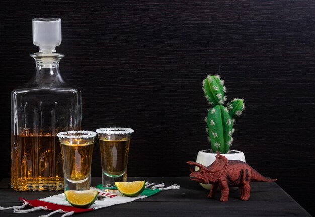 Mexikanische Tequila-Shots, begleitet von einer luxuriösen quadratischen Flasche auf einem Holztisch mit Zitronen