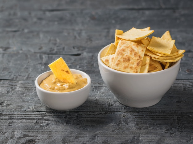 Mexikanische Tortillachips mit Käse in einer weißen Schüssel auf einem schwarzen Holztisch.