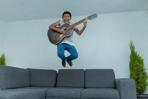 Mexikanischer junge, der vom sofa springt und gitarre spielt