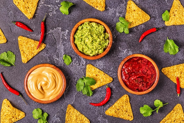 Foto mexikanischer lebensmittelhintergrund: guacamole, salsa, käsesaucen mit zutaten auf schwarzem hintergrund, draufsicht.