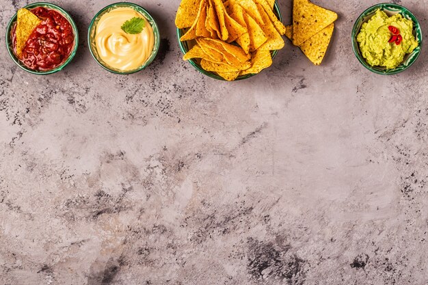 Mexikanischer Lebensmittelhintergrund: Guacamole, Salsa, käsige Soßen mit Nachos, Draufsicht.