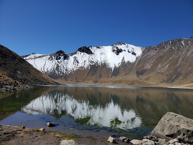 Mexikanischer Vulkan, der durch Schnee bedeckt ist und an einem sonnigen Tag auf einem See reflektiert