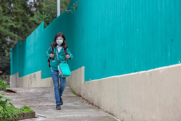 Mexikanisches kleines Mädchen, das nach der Coronavirus-Pandemie mit Gesichtsmaske zurück zur Schule geht