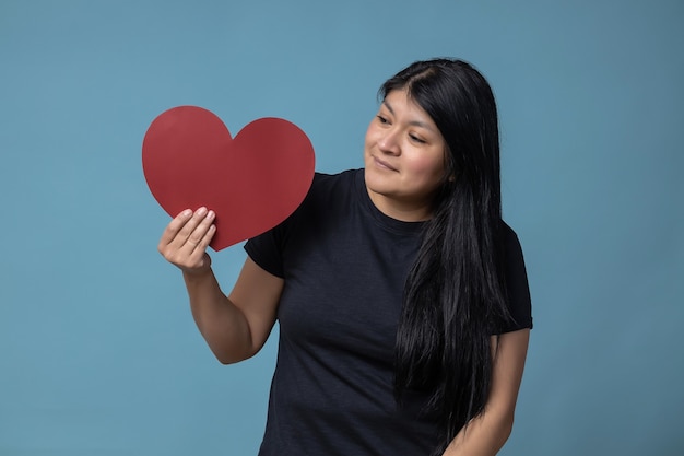 Mexikanisches lateinamerikanisches Mädchen, das einen Valentinstag eines roten Herzformpapiers hält