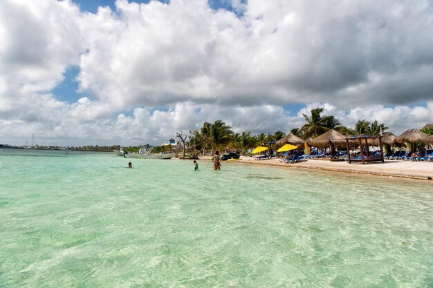 Mexiko, Costa Maya - 1. Februar 2016: tropischer Strand und Menschen in transparentem Meer- oder Ozeanwasser mit Sonnenliegen auf weißem Sand mit grünem Palmen-Touristenort am sonnigen Sommertag am bewölkten Himmel