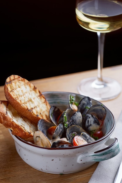 Foto mexilhões com pão grelhado e copo de vinho branco na mesa de madeira saboroso conceito de frutos do mar com fundo escuro