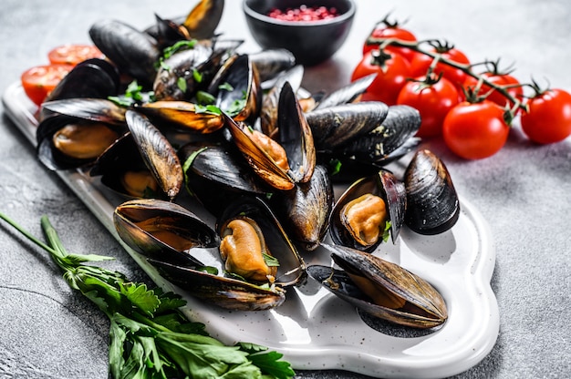 Mexilhões crus com conchas em uma tábua. o conceito de cozinhar frutos do mar em molho de tomate com salsa. fundo cinza. vista do topo