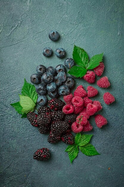 una mezcla de bayas maduras con hojas esparcidas en la mesa frambuesas moras arándanos